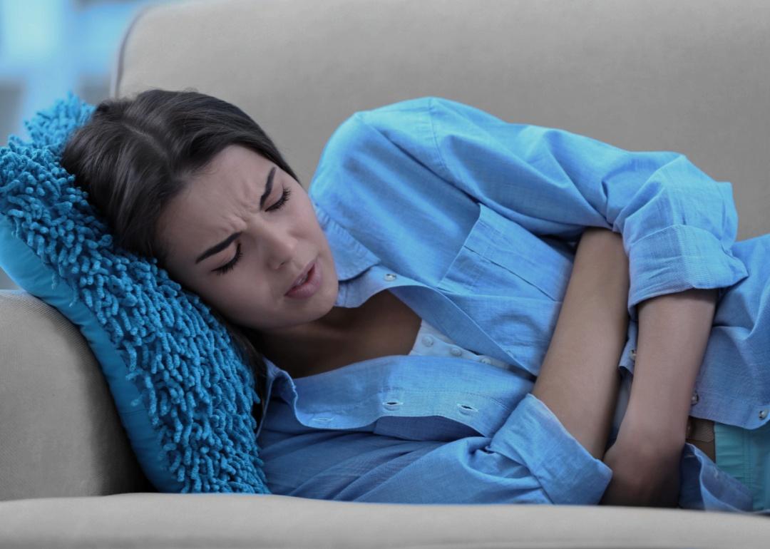 Young woman lying on sofa with closed eyes and holding her stomach.