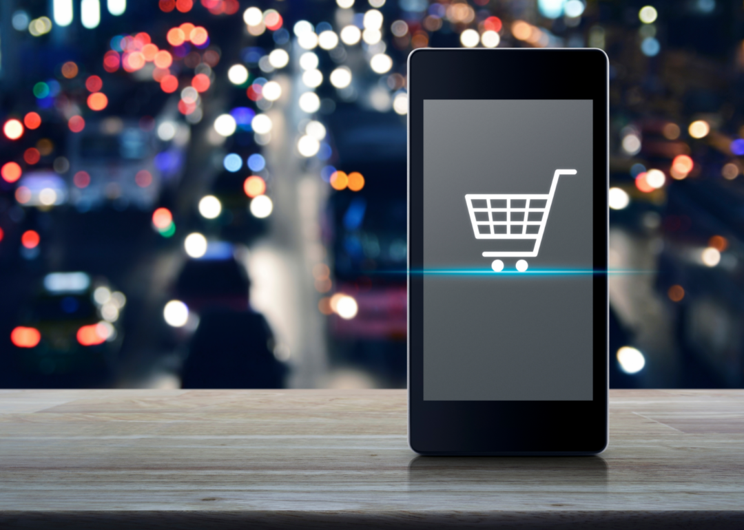 A shopping cart appears on a phone screen with city lights in the background.