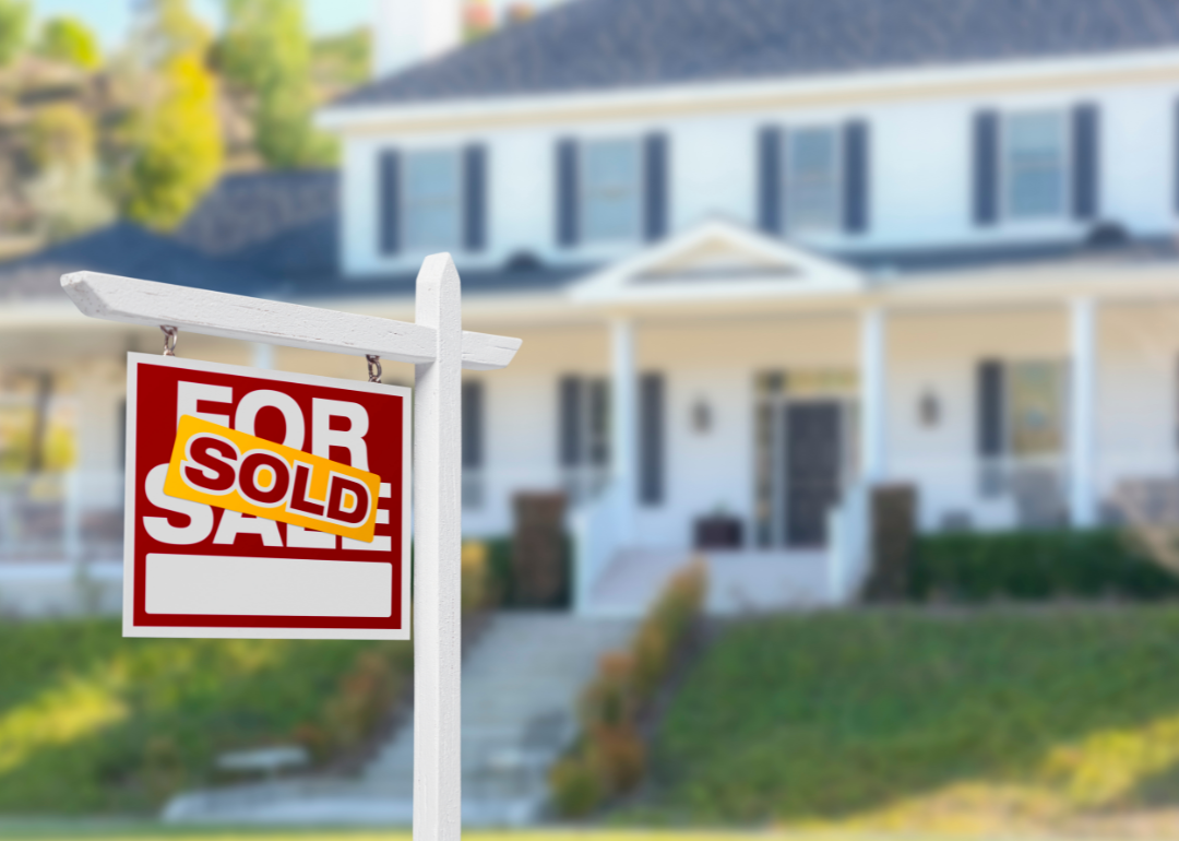 A for sale sign with a sold sticker in front of a suburban home.