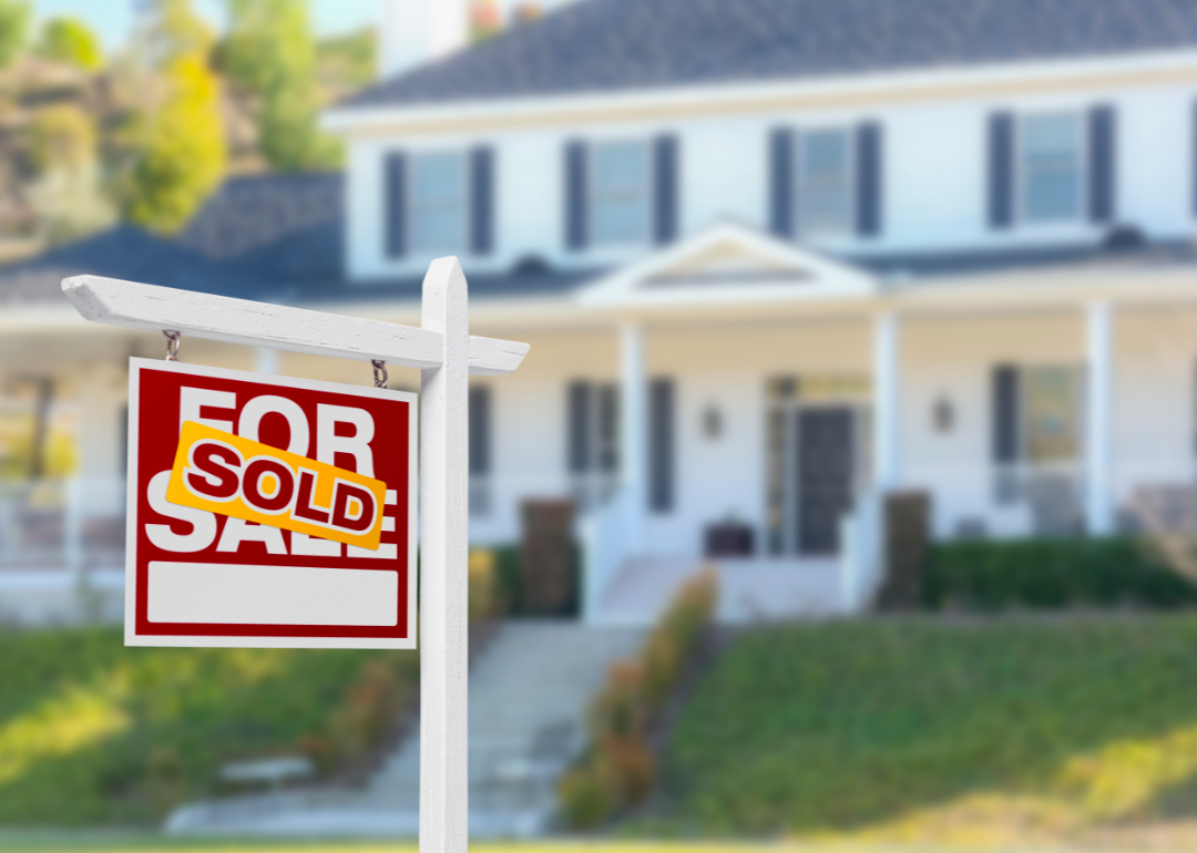 A for sale sign with a sold sticker on it in the front lawn of a midsize suburban home.