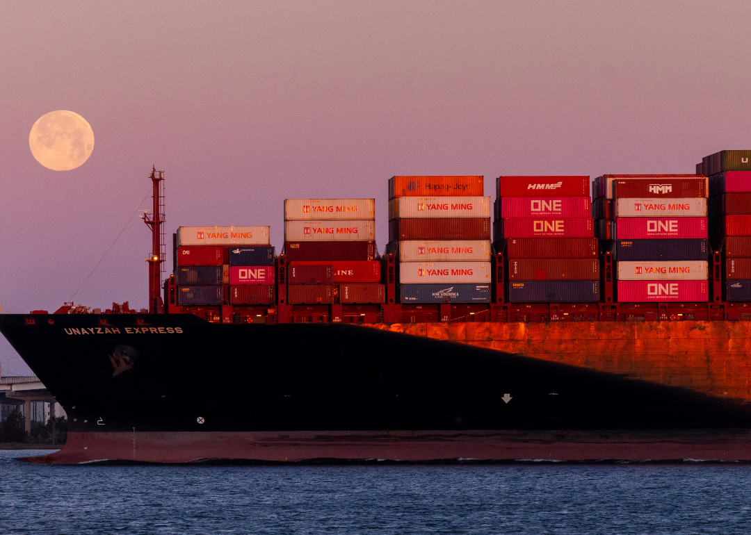 A container ship next to a full moon.