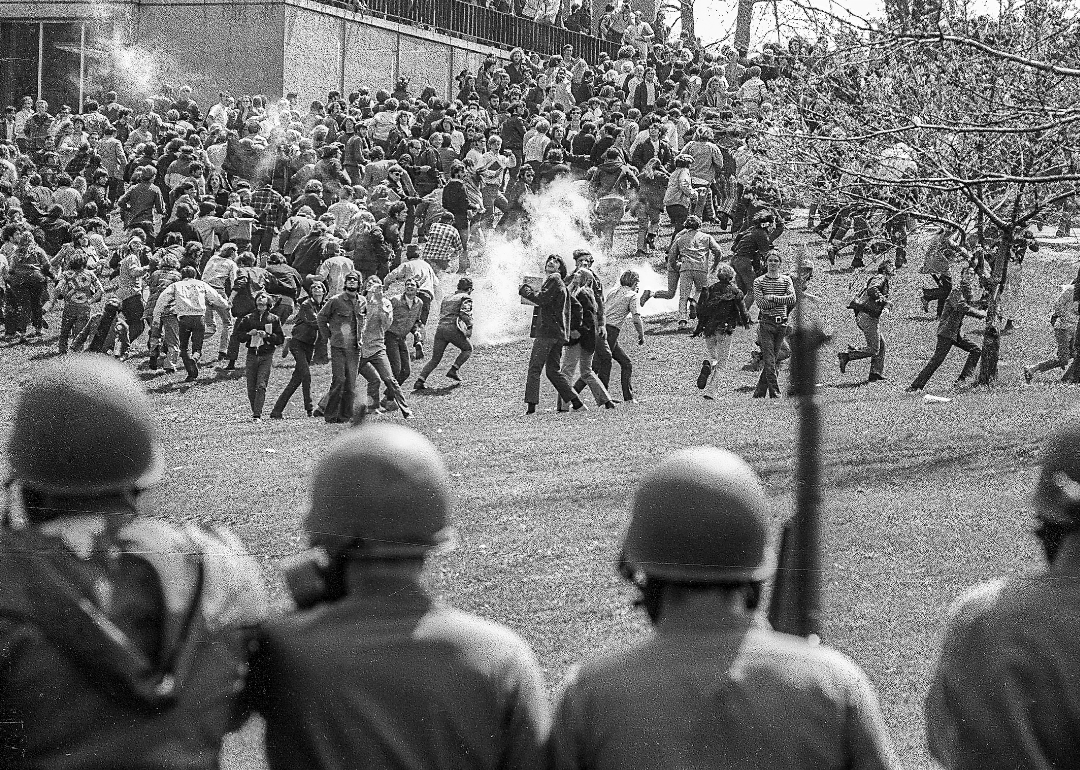 National Guardsmen in gas masks with rifles drive back Kent State University students.