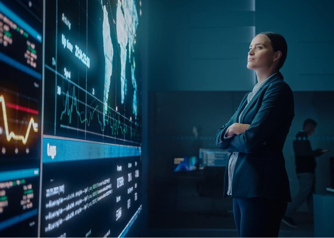 A young woman looking at big screen display showing global map with data points.