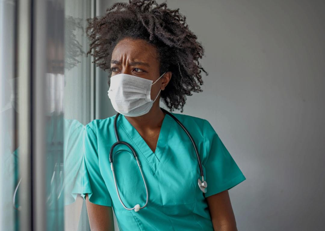 A masked female nurse looking distressed.