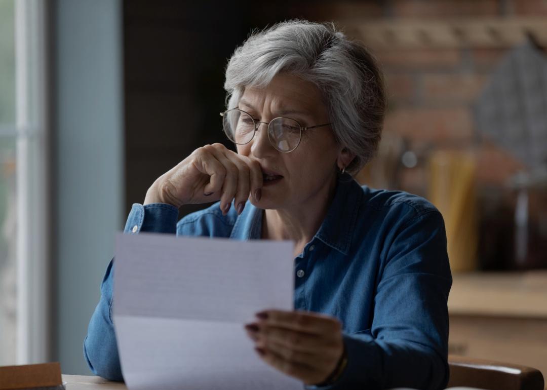 An older woman looking at the sheet of paper in her hand looking distressed and concerned.