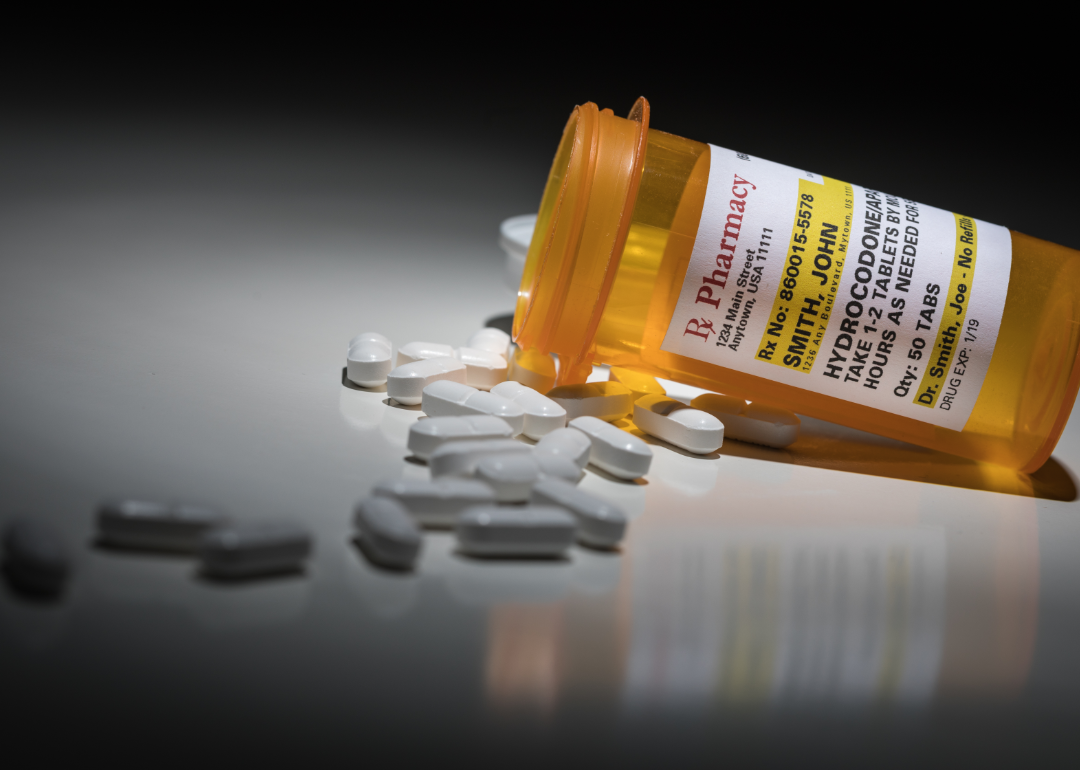 A prescription bottle for Hydrocodone on its side with pills spilling out.