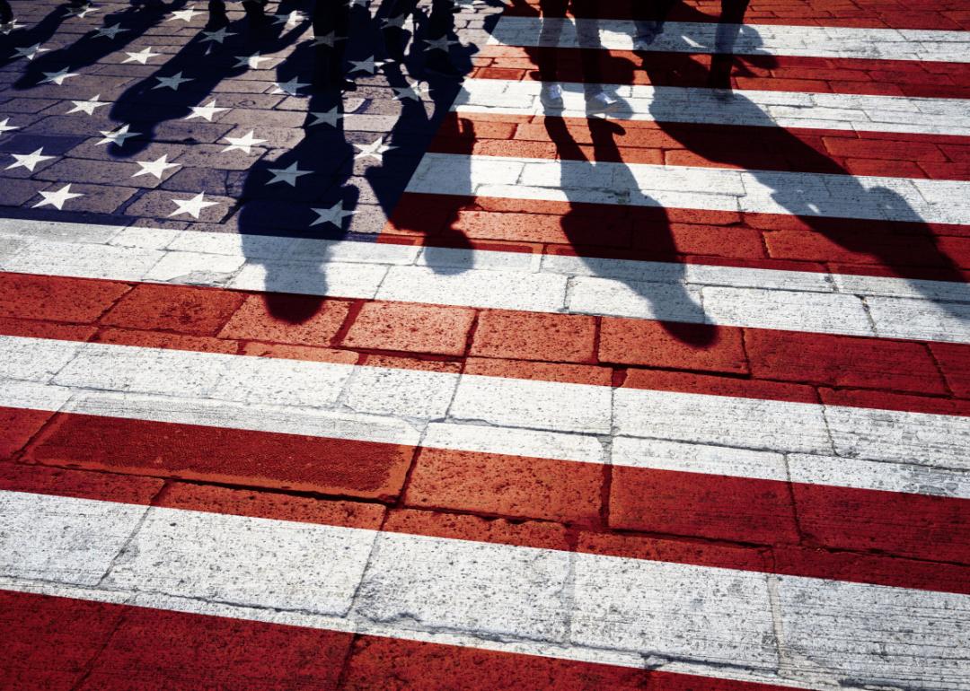 Shadows of group of people walking through the sunny streets with painted United States of America flag on the floor.