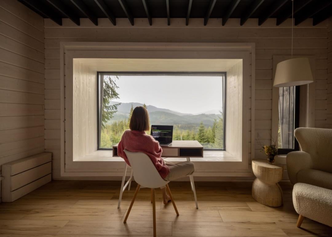A woman working at a desk looking out on green mountains.