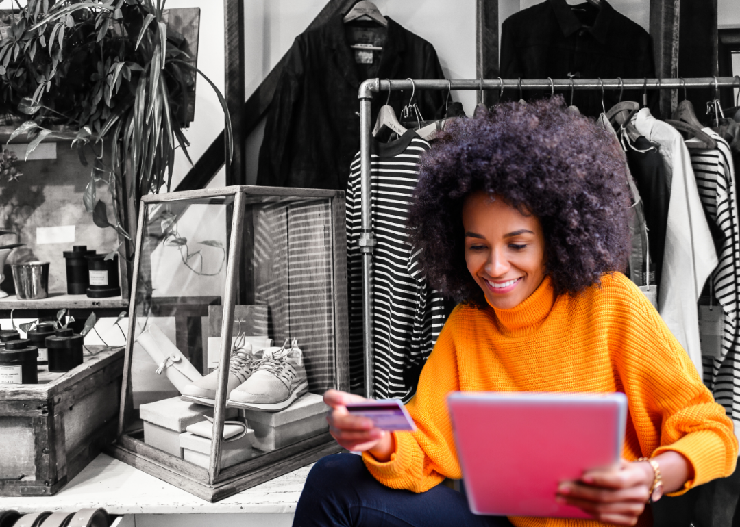 A woman shopping online in front of a black-and-white image of a clothing store.