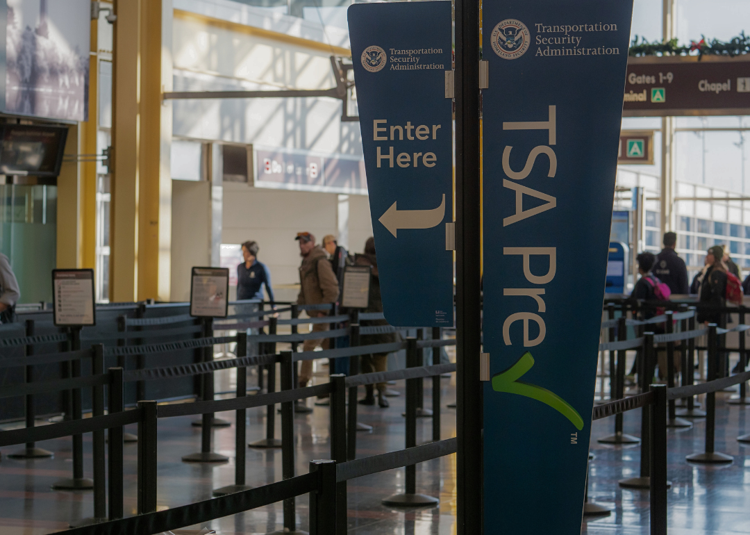 Two blue signs with white lettering suspended on a pole at an airport. Large one says "Transportation Security Administration TSA Pre" and the smaller one says 'Transportation Security Administration enter here.'