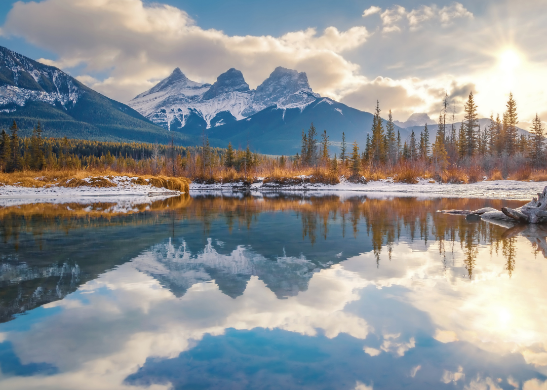 Three snowy mountain peaks reflected in the body of water in the foreground.