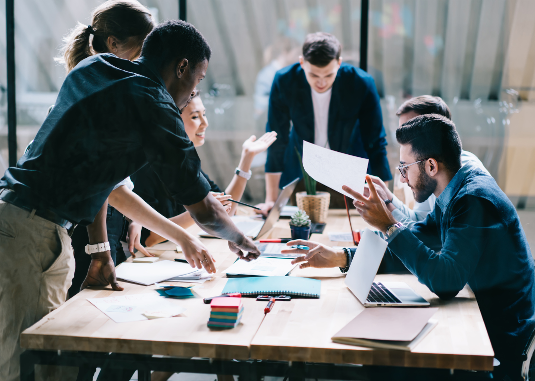 A group of businesspeople surrounding a table brainstorming.