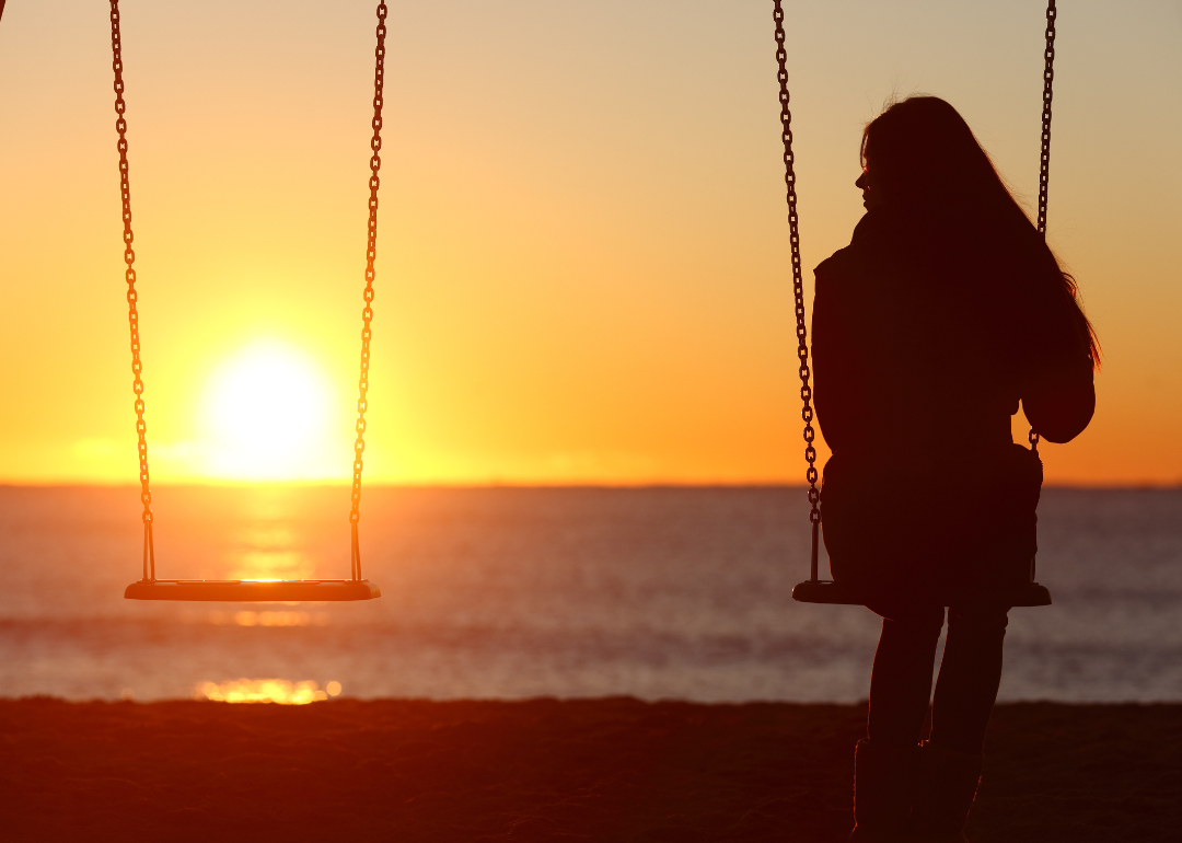 A young person sitting alone on a pair of swings near the beach