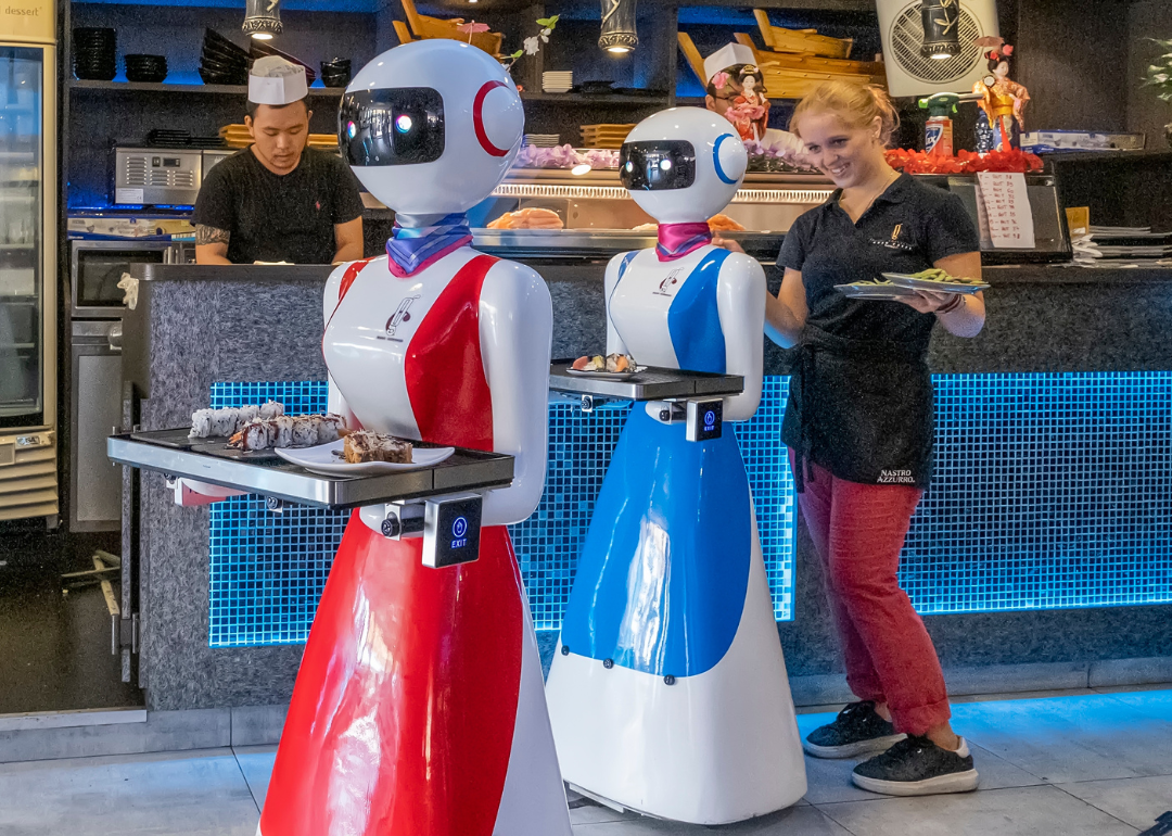 Robot waiters bringing orders to guests alongside people.