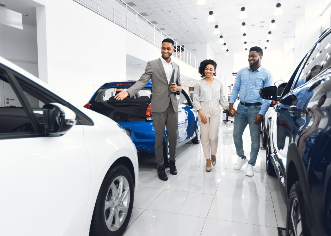 A salesman showing luxury cars to a couple at a car dealership