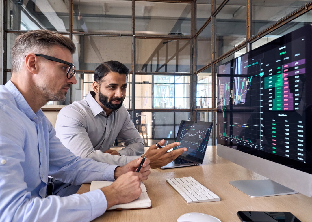 Two financial workers looking at graphs and talking at their desks