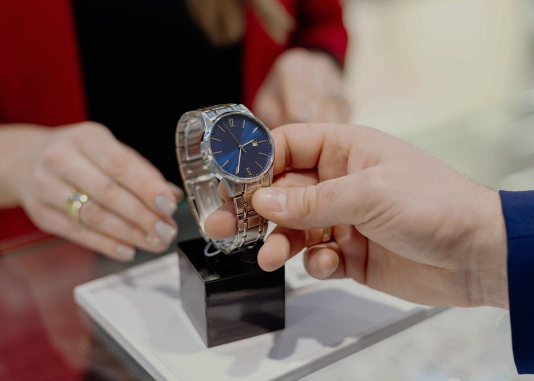 A closeup of man's hands touching a watch on a black stand. 