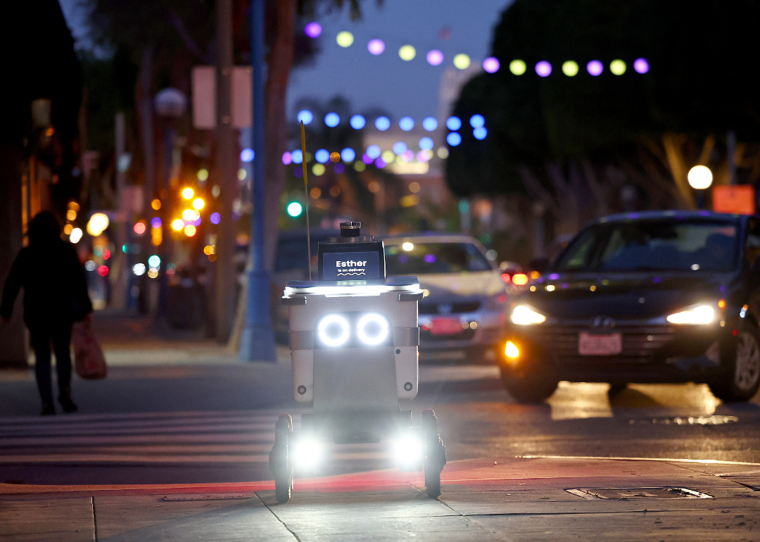 An autonomous robot with the name Esther displayed on its screen making a delivery in the city.