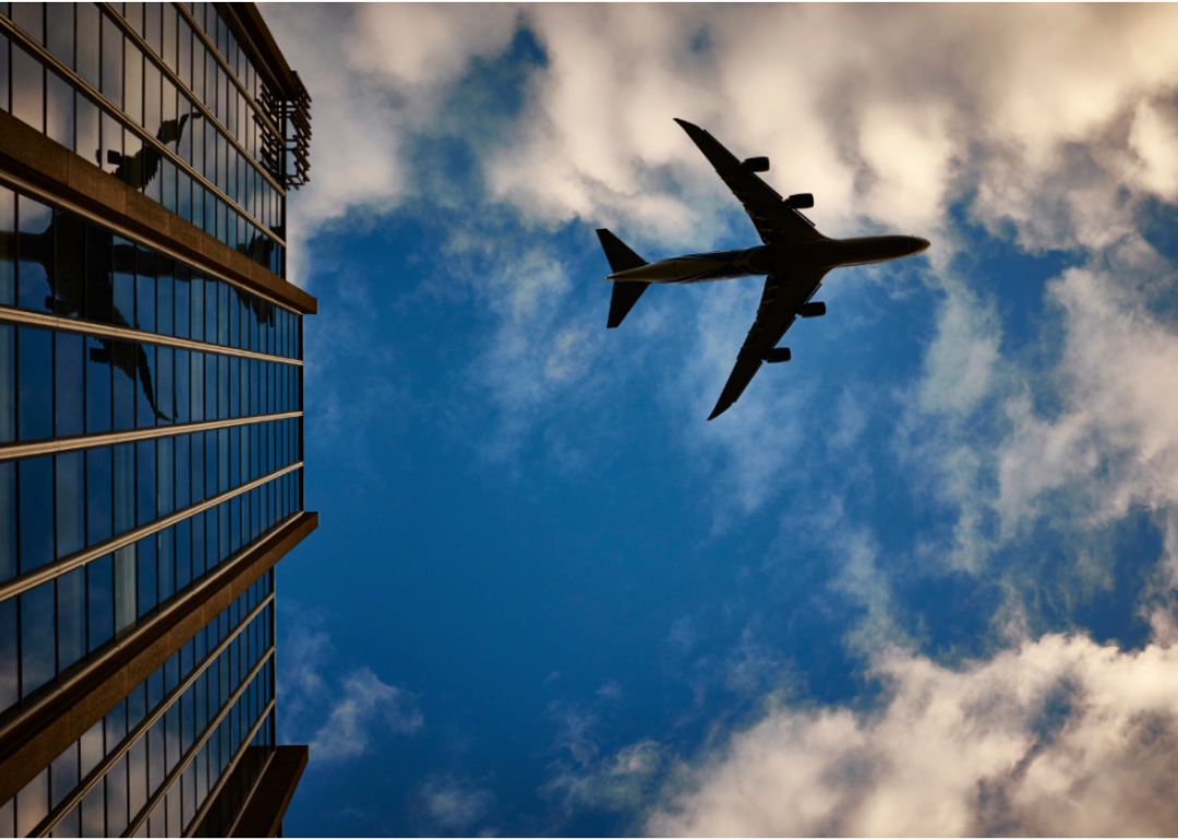 A silhouette of a airliner against blue skies, reflected in a tall building.