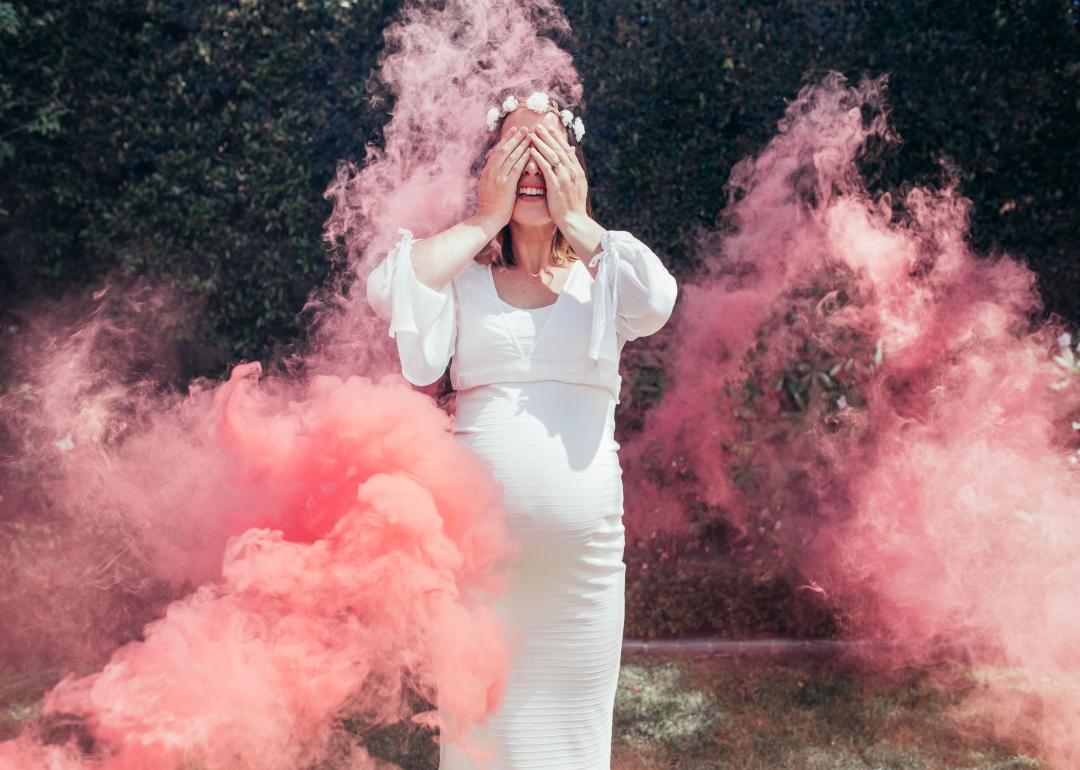 A woman covering her eyes with pink smoke rising around her.