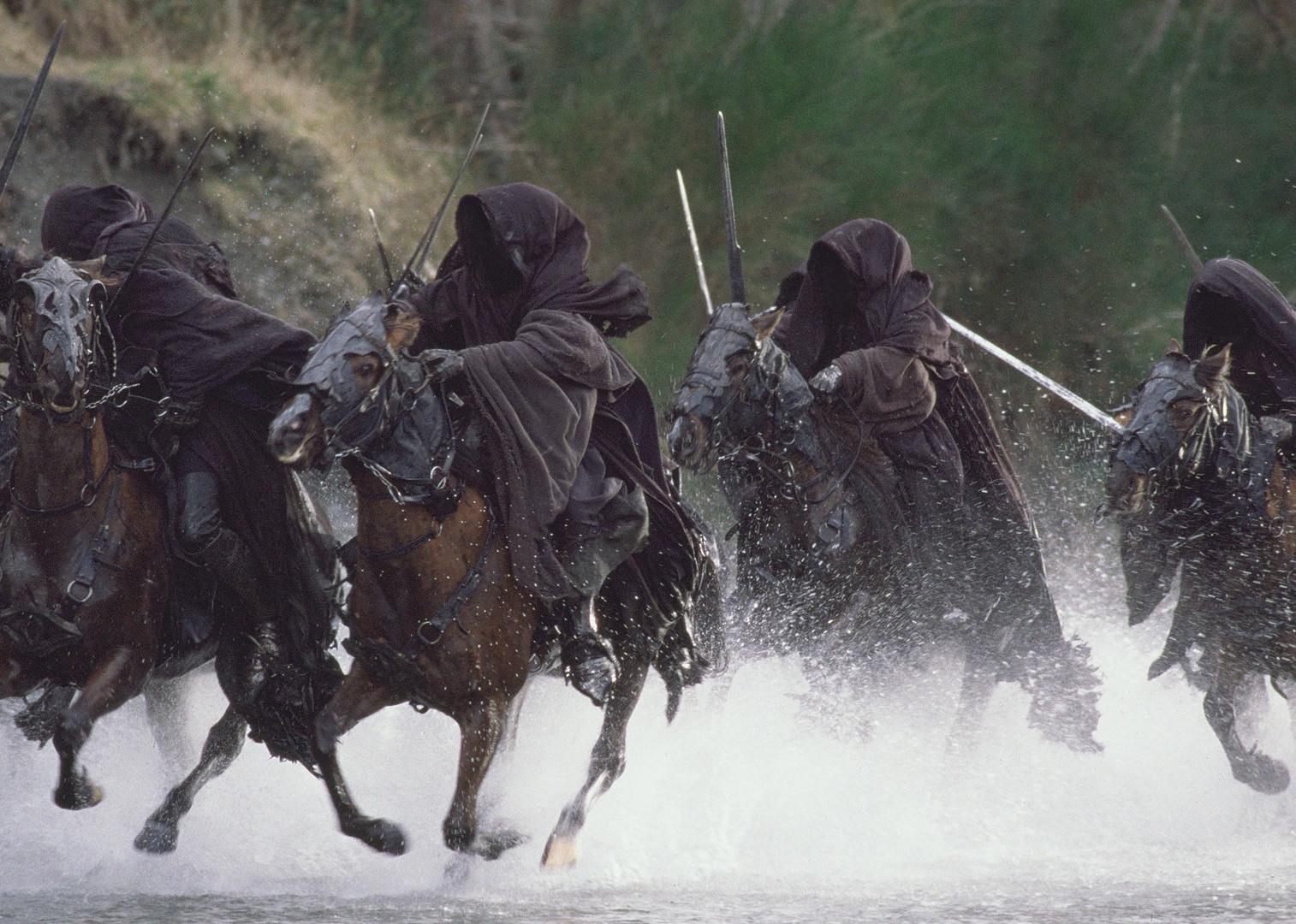 Horses run through water with riders who have their heads covered in black cloth.