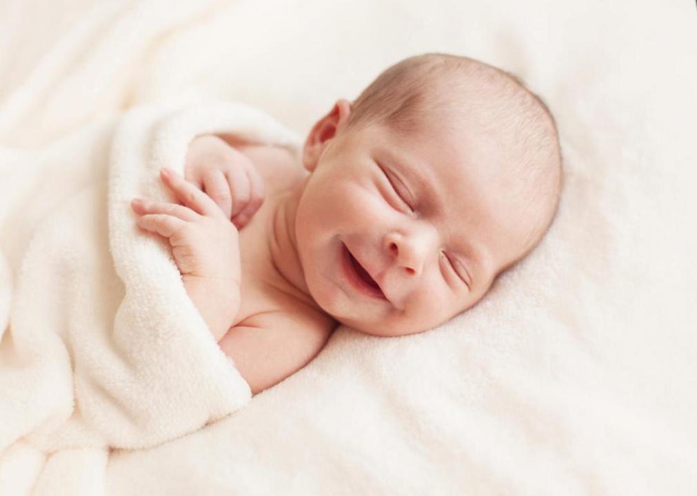 Smiling baby wrapped in white blanket.