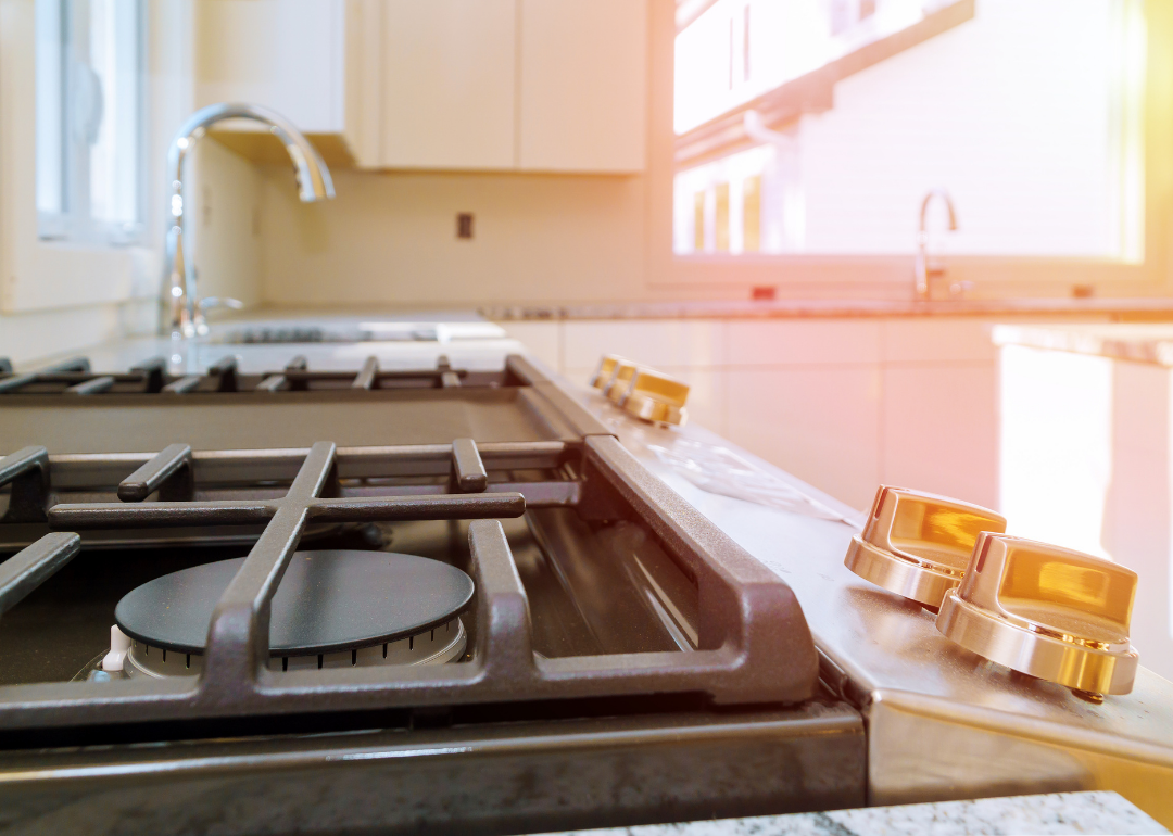 Close-up of gas range with pink and yellow light coming in the kitchen window.