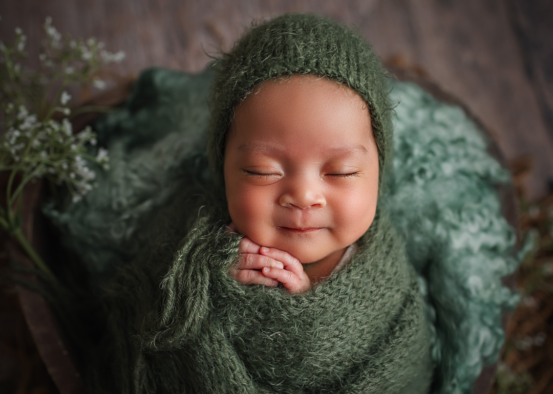 A smiling baby sleeping in a green knit cap and swaddle.