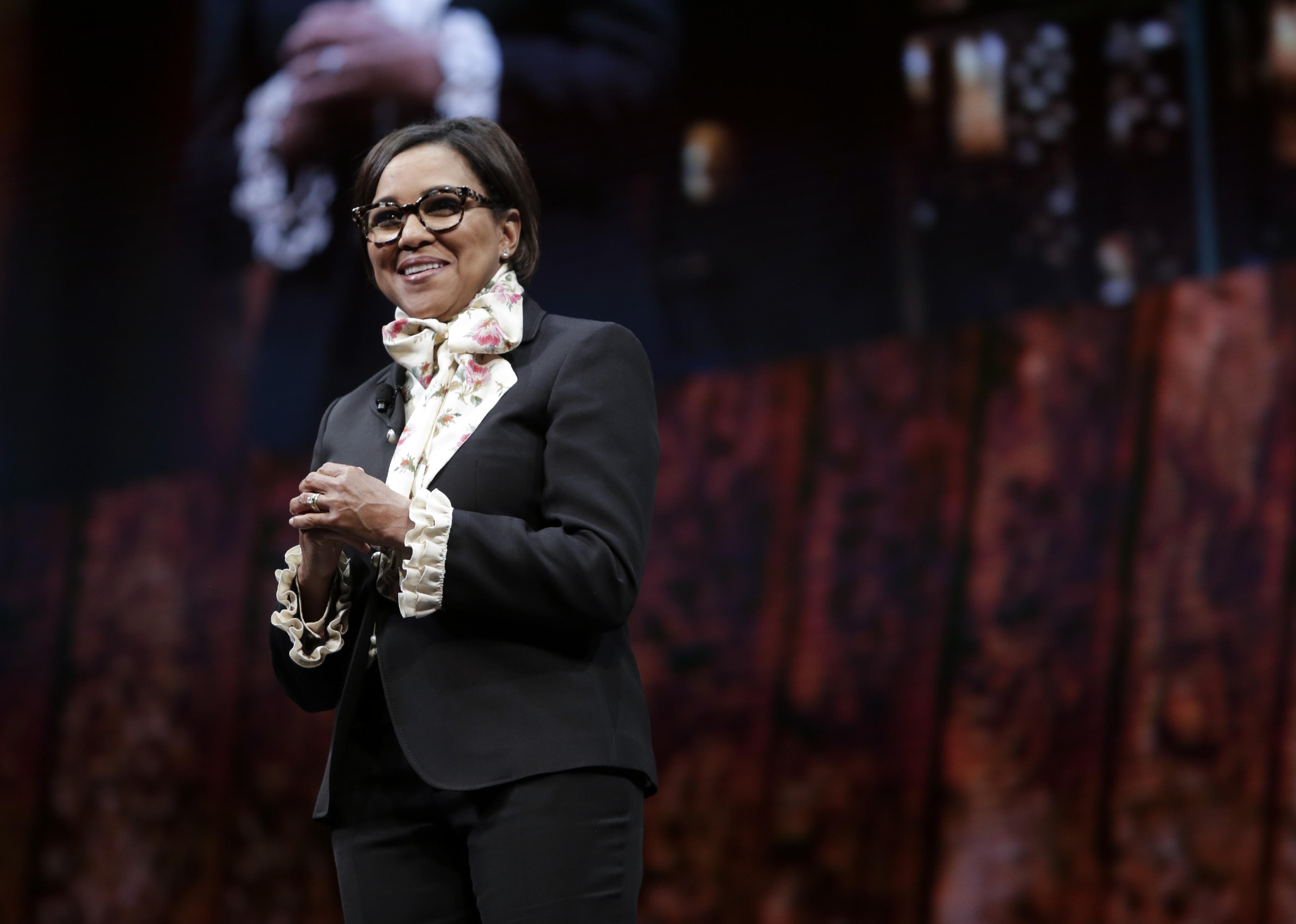 Roz Brewer speaking onstage in a black suit with a floral top accent.