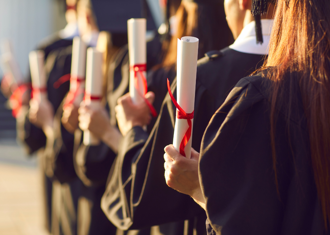 College graduates standing in a line holding diplomas.