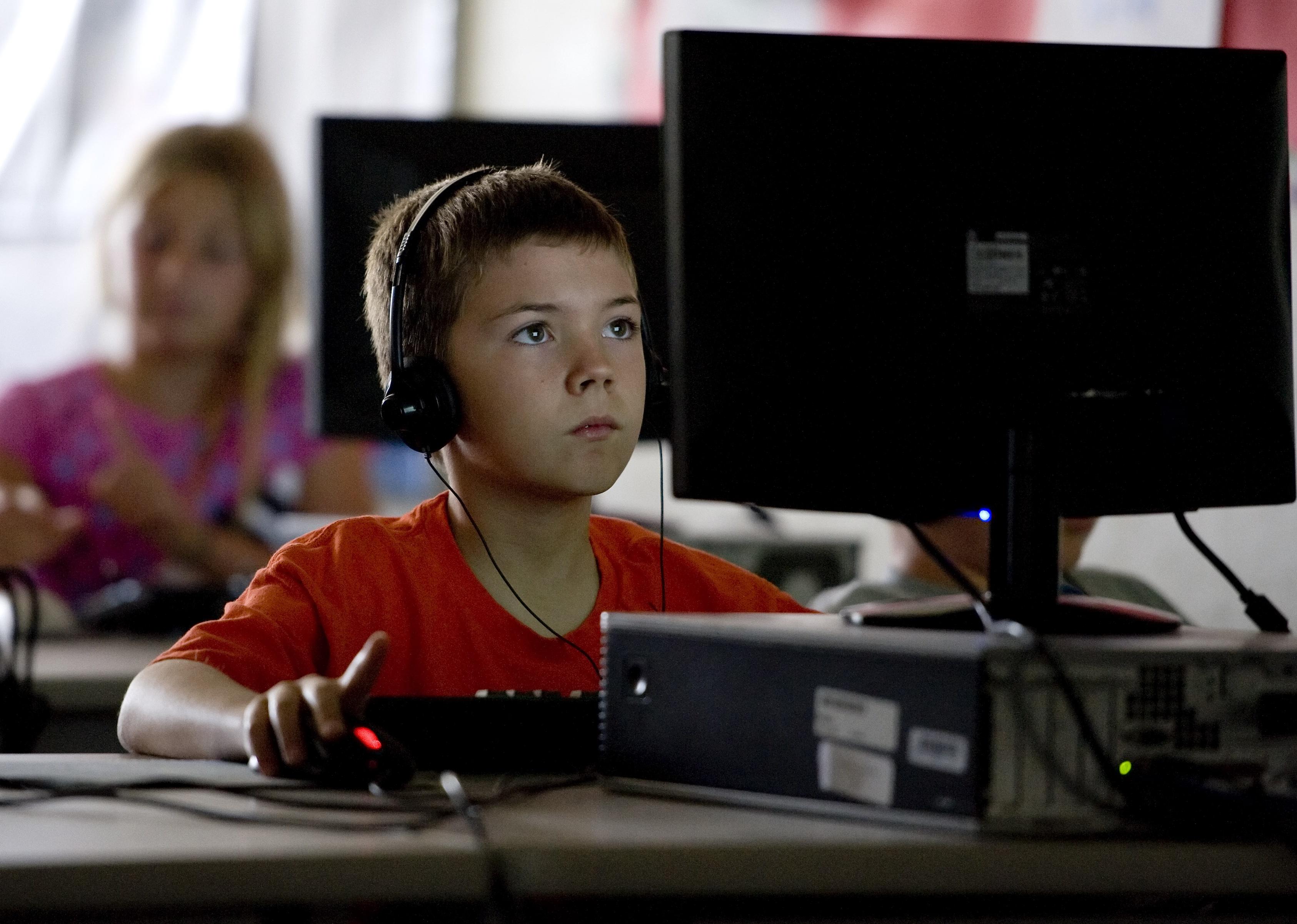 A third grade student sits at a computer working while wearing headphones.