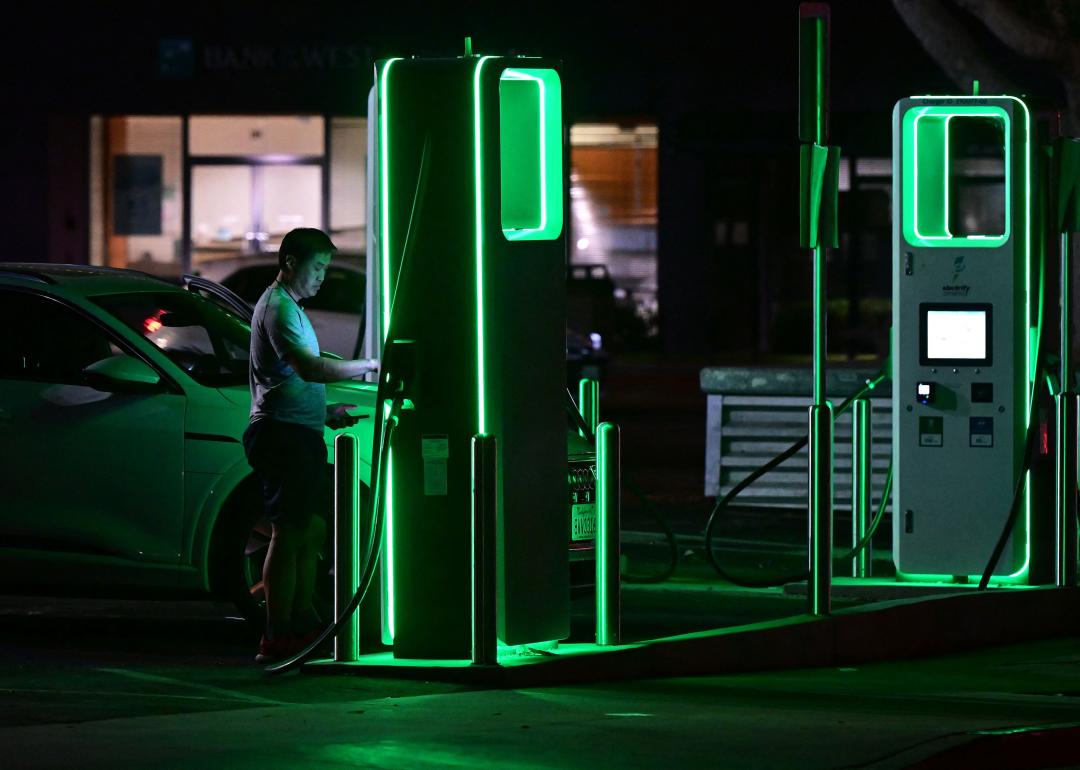 A man setting up his electric car to charge at a green lit charging station at night.