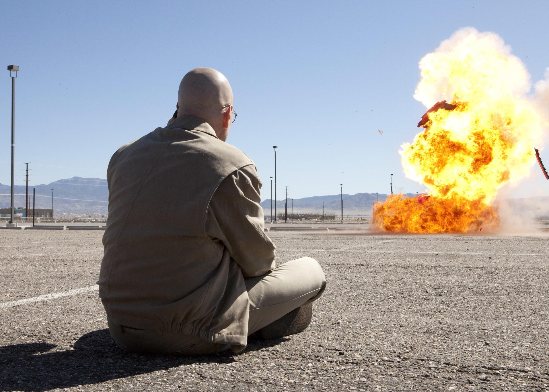 Bryan Cranston sitting on the pavement watching an explosion.
