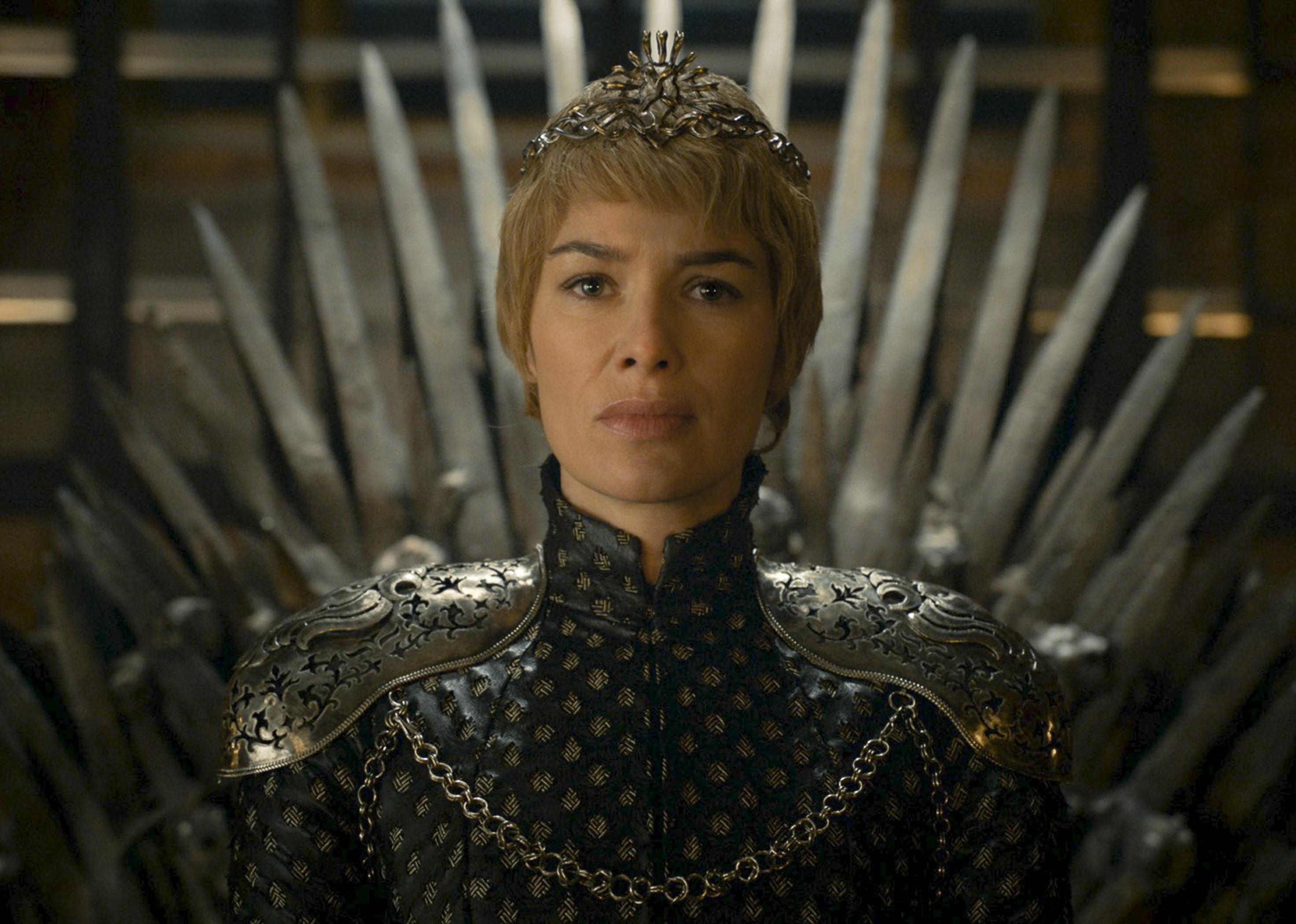 Lena Headey, with short hair, in armor and a crown on a throne.