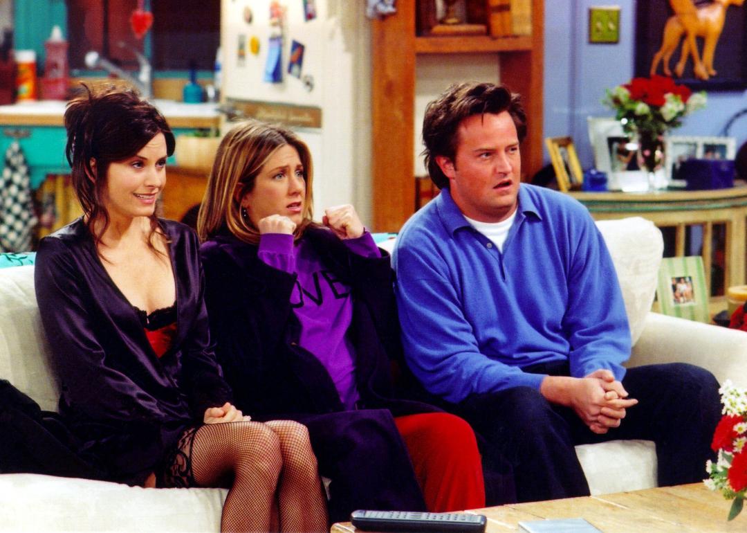 Courteney Cox, Jennifer Aniston and Matthew Perry sitting on the couch in Monica's living room in a scene from Friends. 