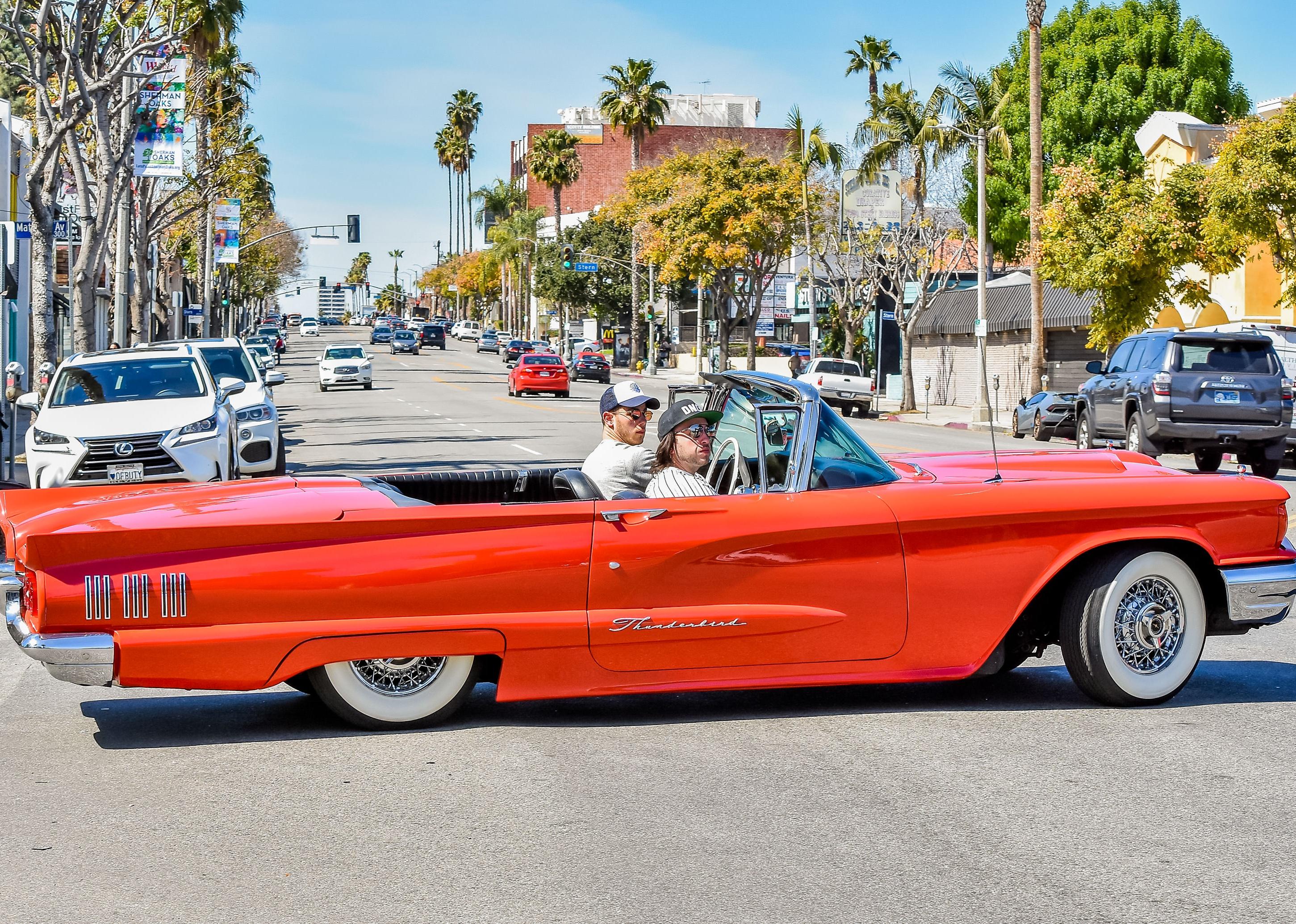 Nick Jonas driving a red convertible.