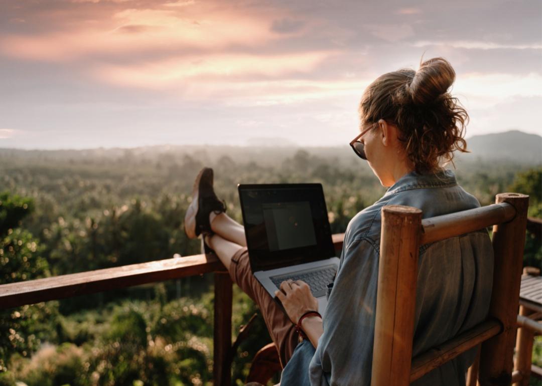 A woman working outside on a balcony on a laptop with her feet up.