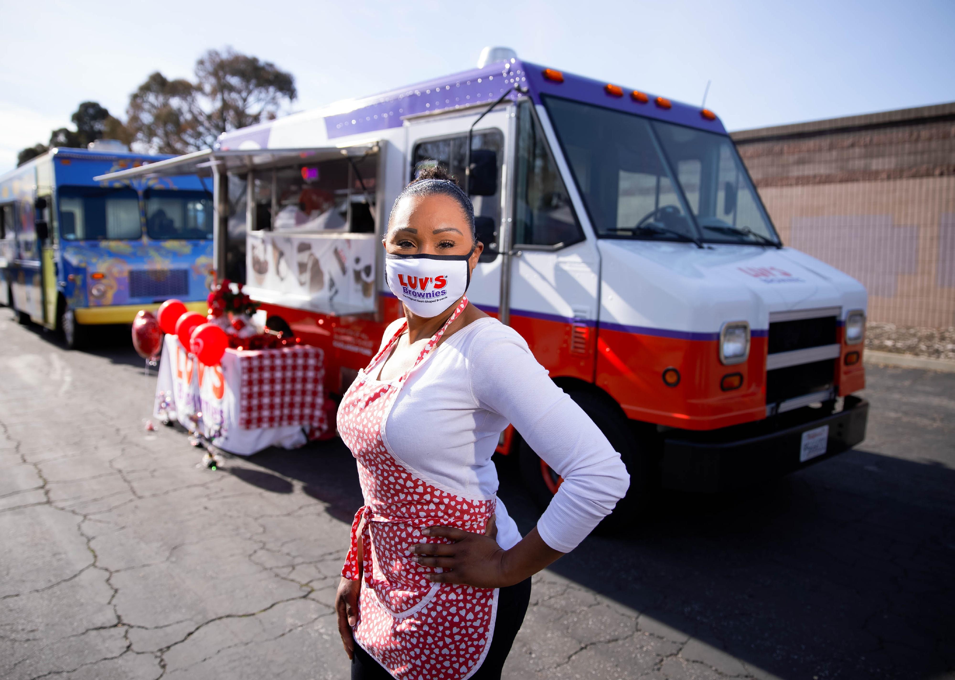 A masked woman stands outside her brownie food truck.