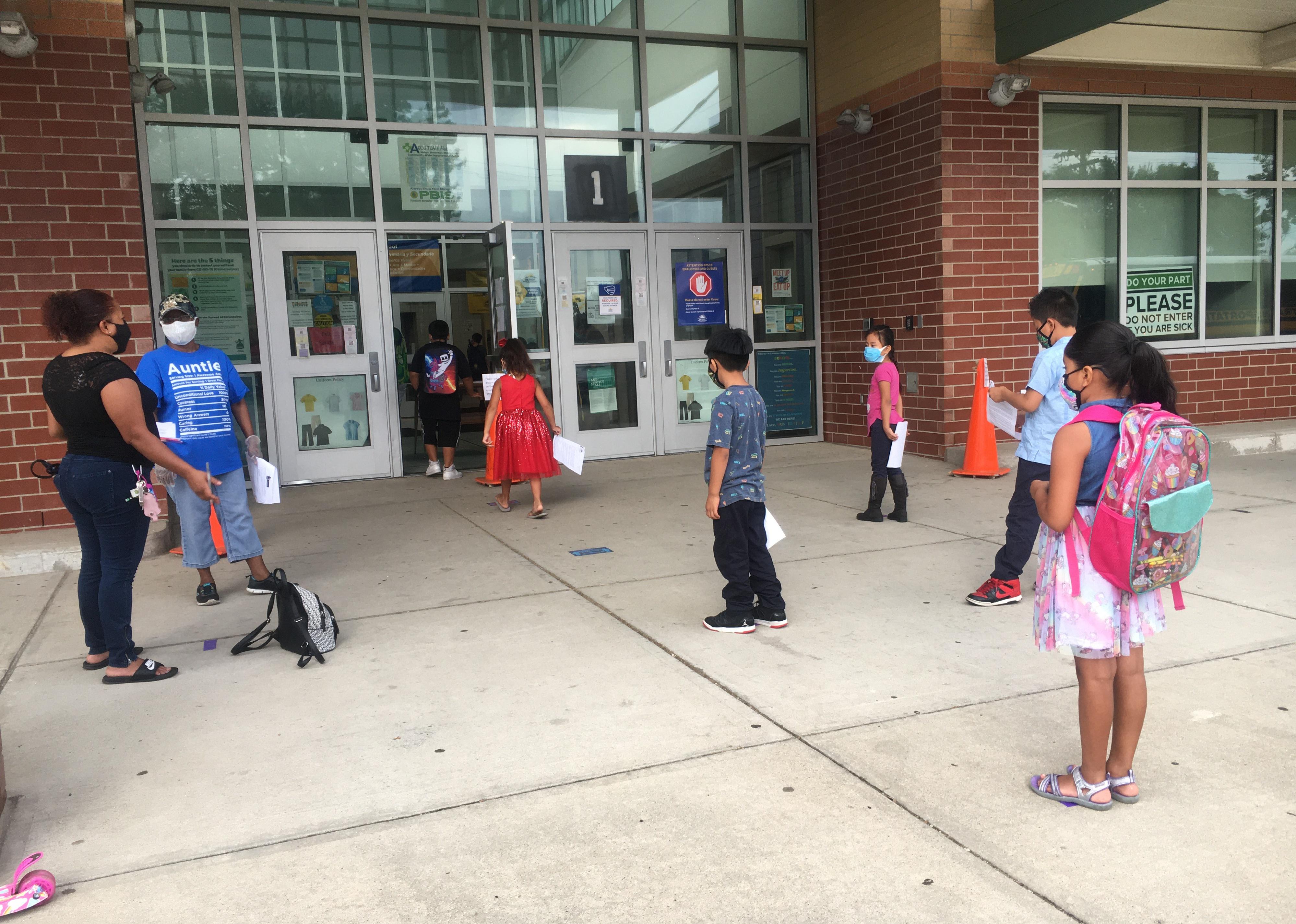 Elementary students stand distanced from one another ready to enter summer school.