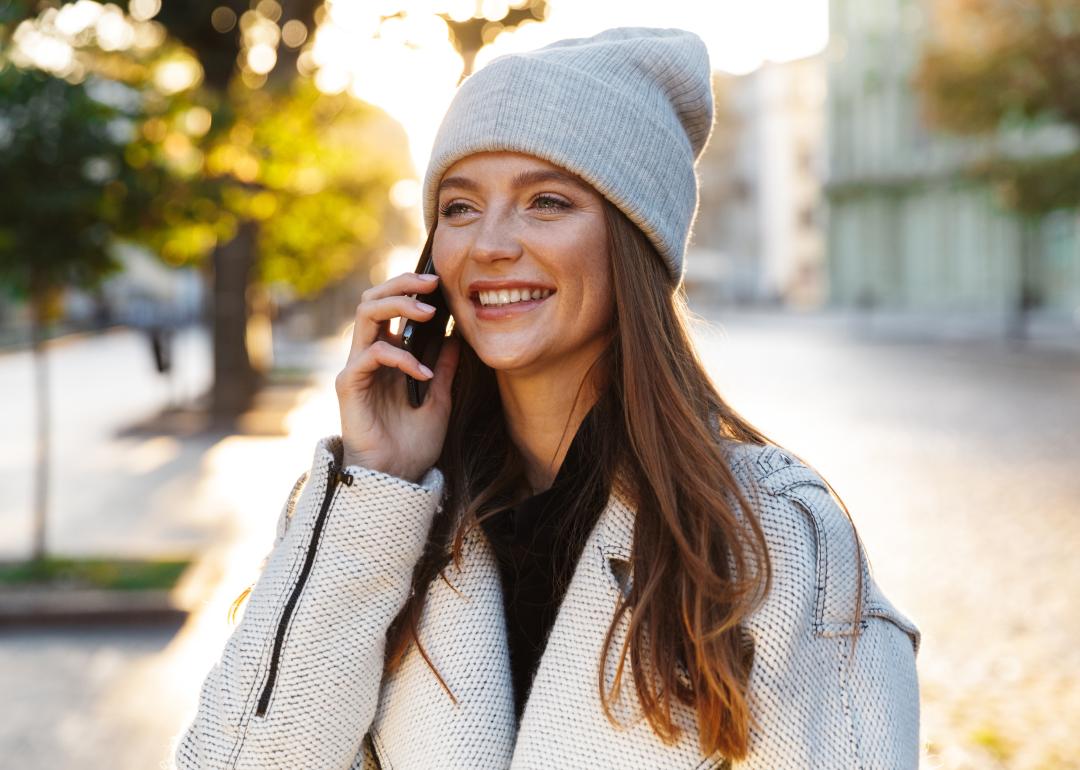 Woman walking outdoors wearing a hat and talking on cell phone.