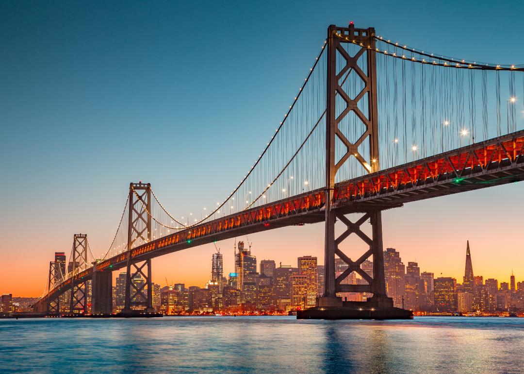View of San Francisco skyline with famous Oakland Bay Bridge illuminated in evening light.
