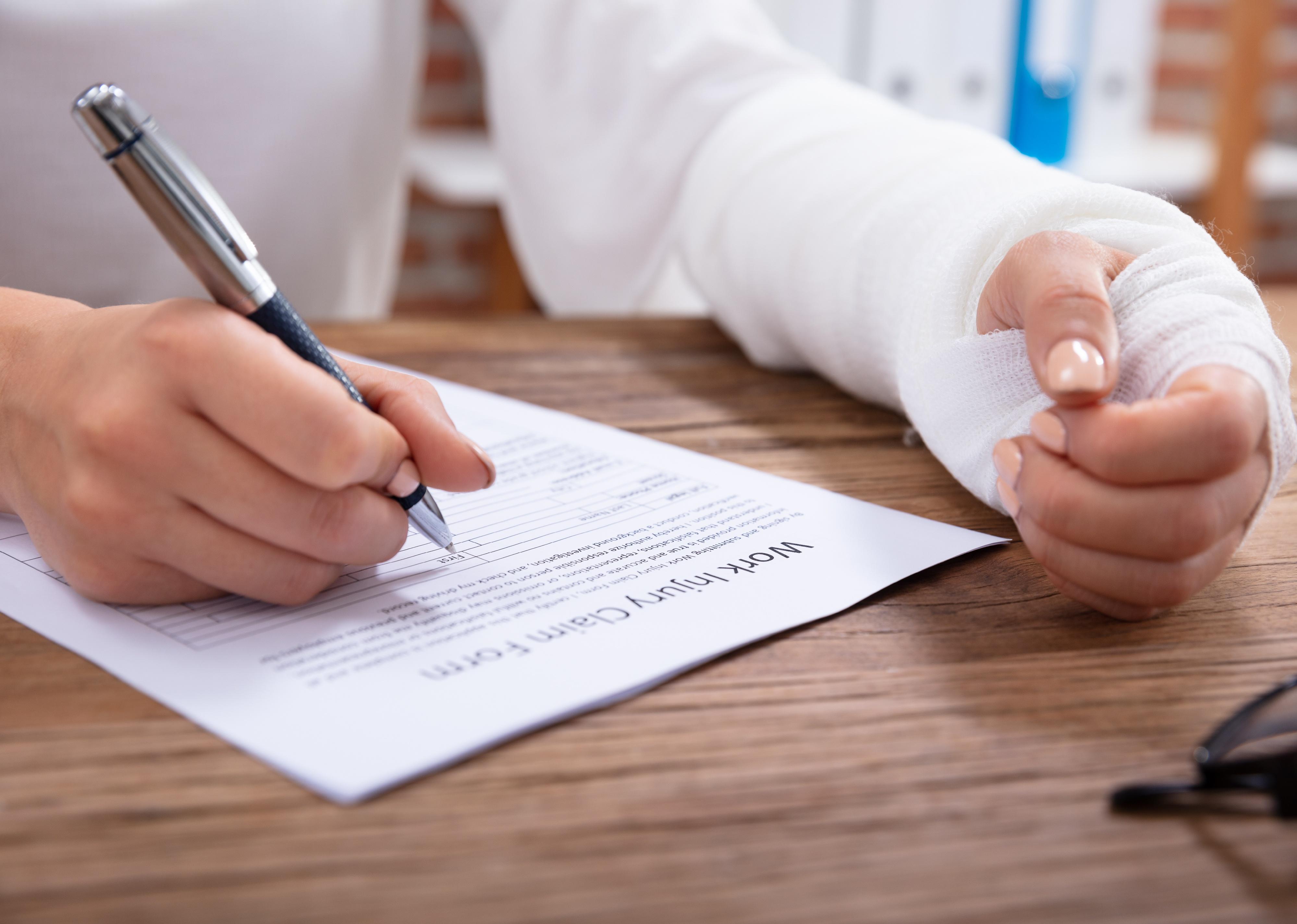 Close-up of woman with bandaged hand filling out claim form