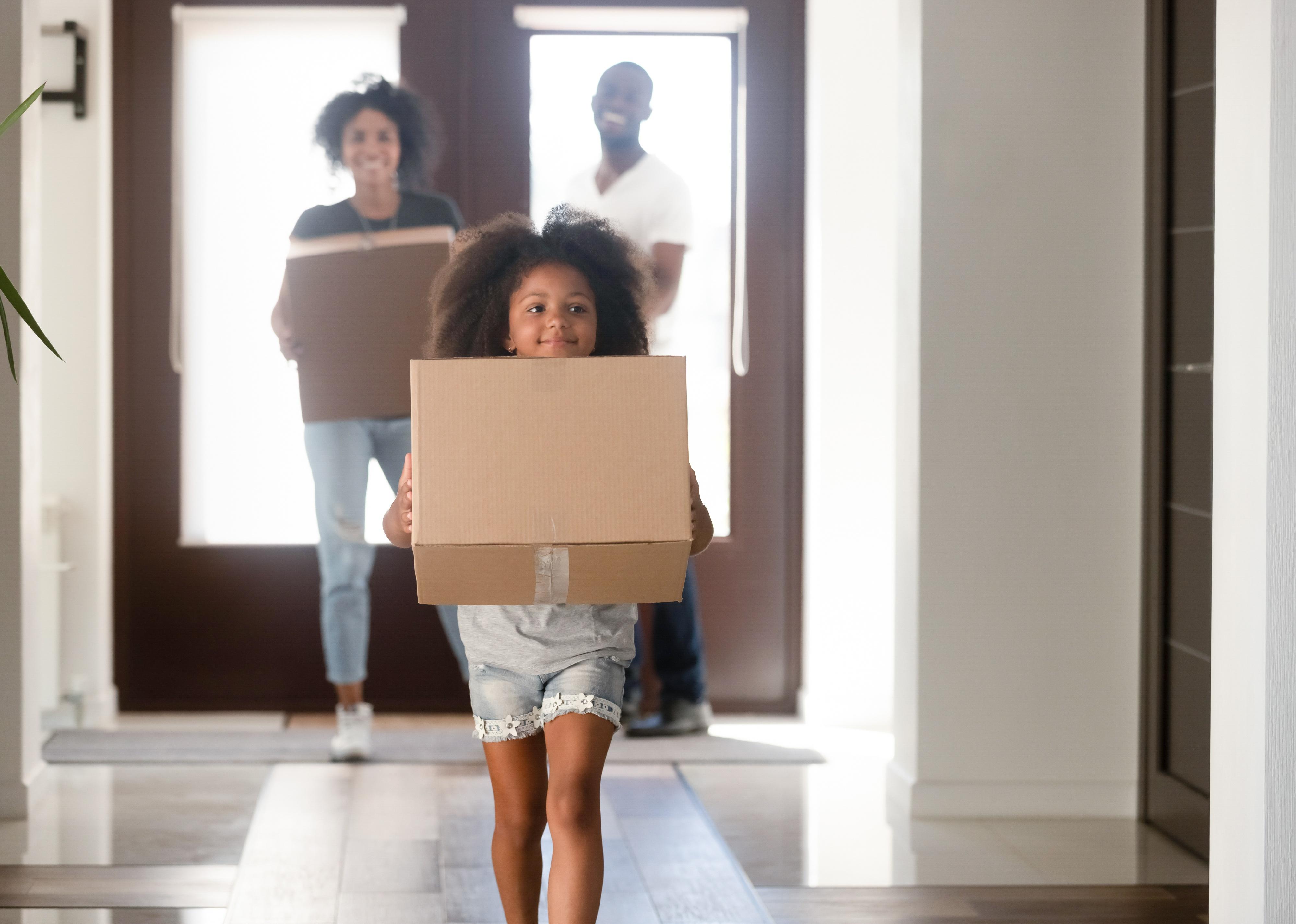 Young girl holding cardboard box running into a house