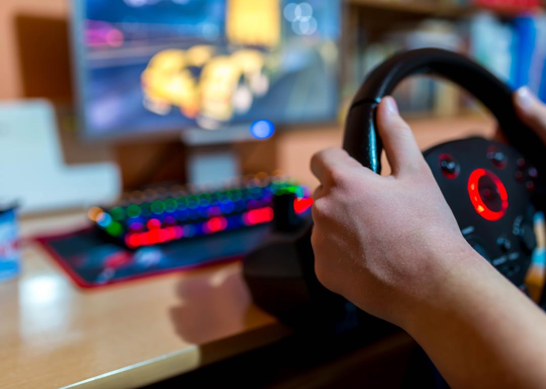 Teenager playing on truck driving simulator in front of a computer.