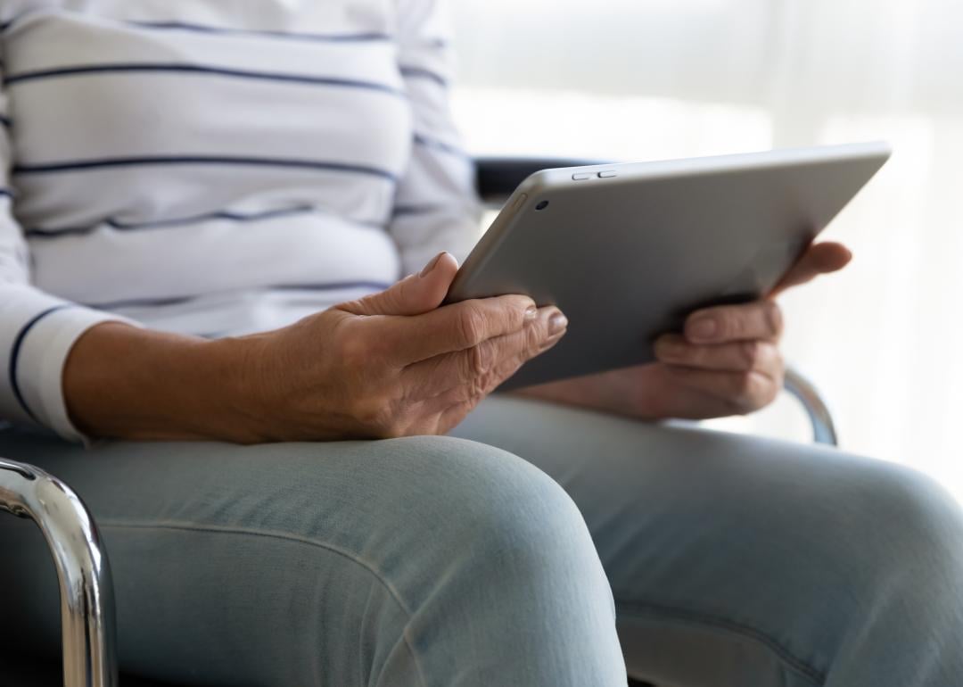 Elderly woman in wheel chair holds a tablet. 