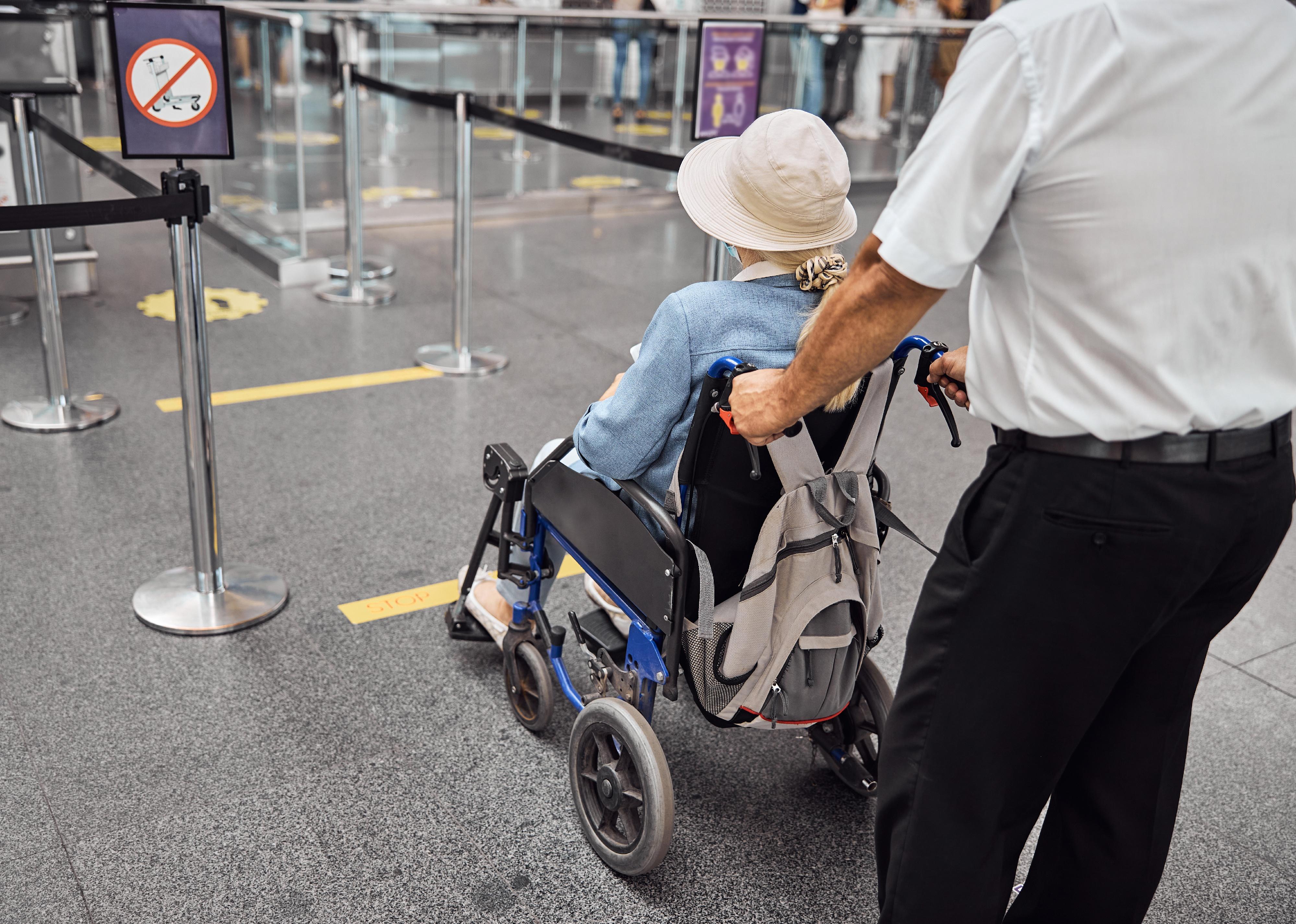 Back view of an airport male employee transporting a disabled female traveler to a plane