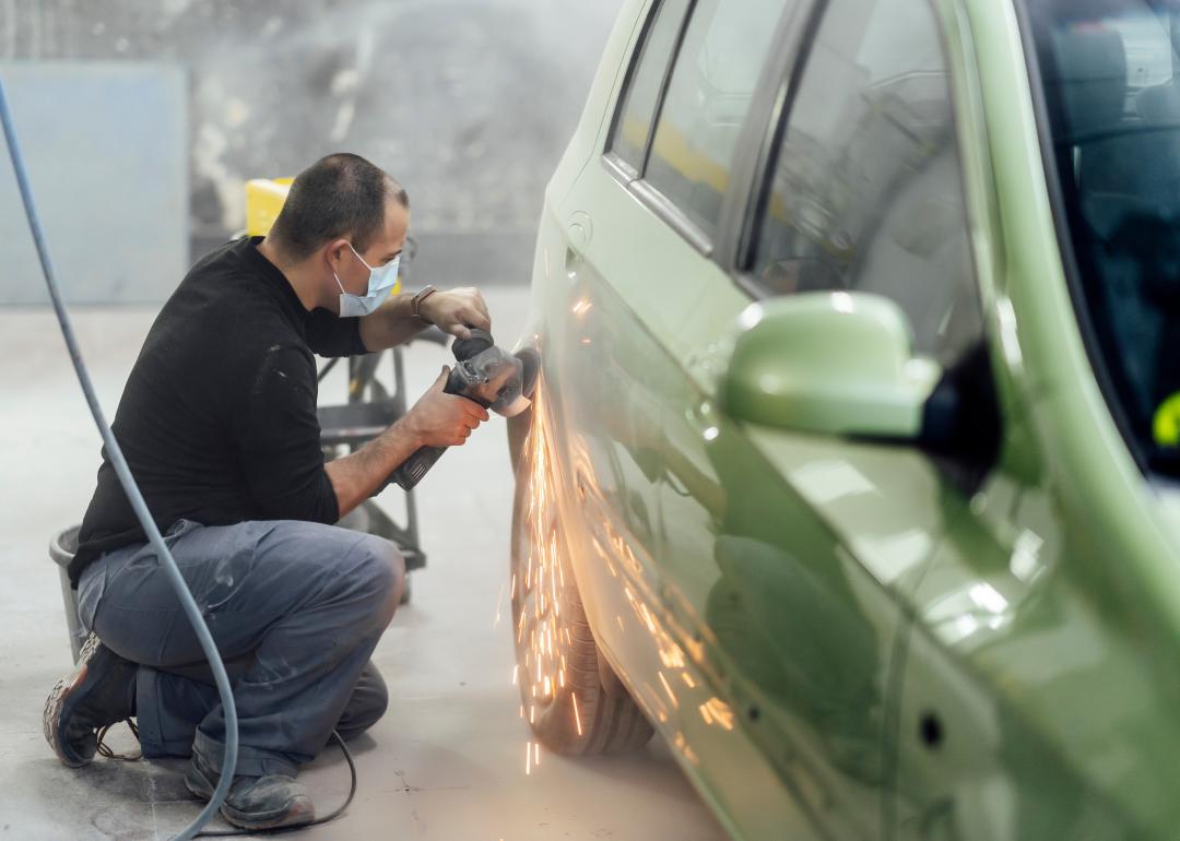 Mechanic working in a workshop sanding a car with radial.