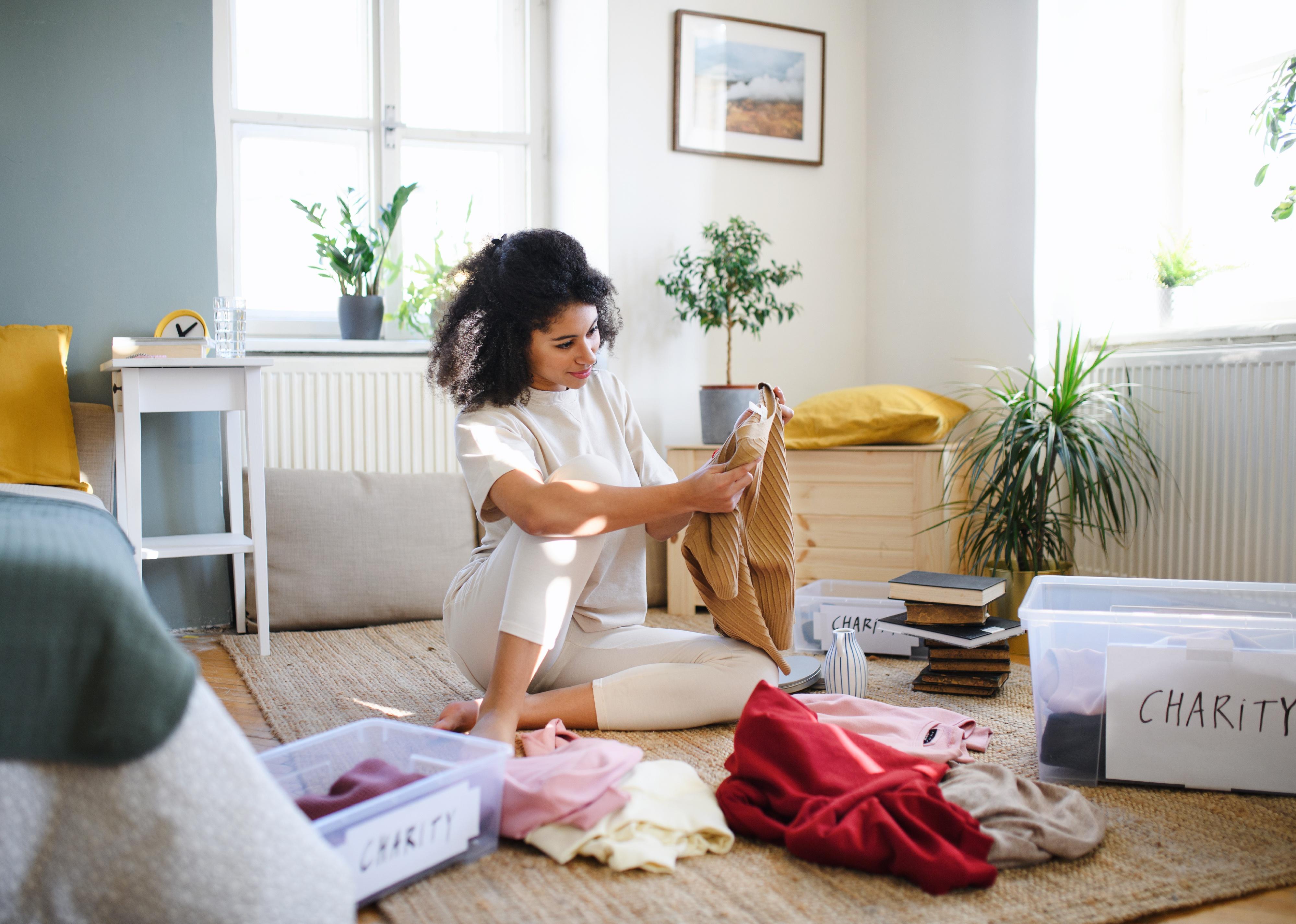 A woman sorts piles of clothes into boxes, both labeled "charity."