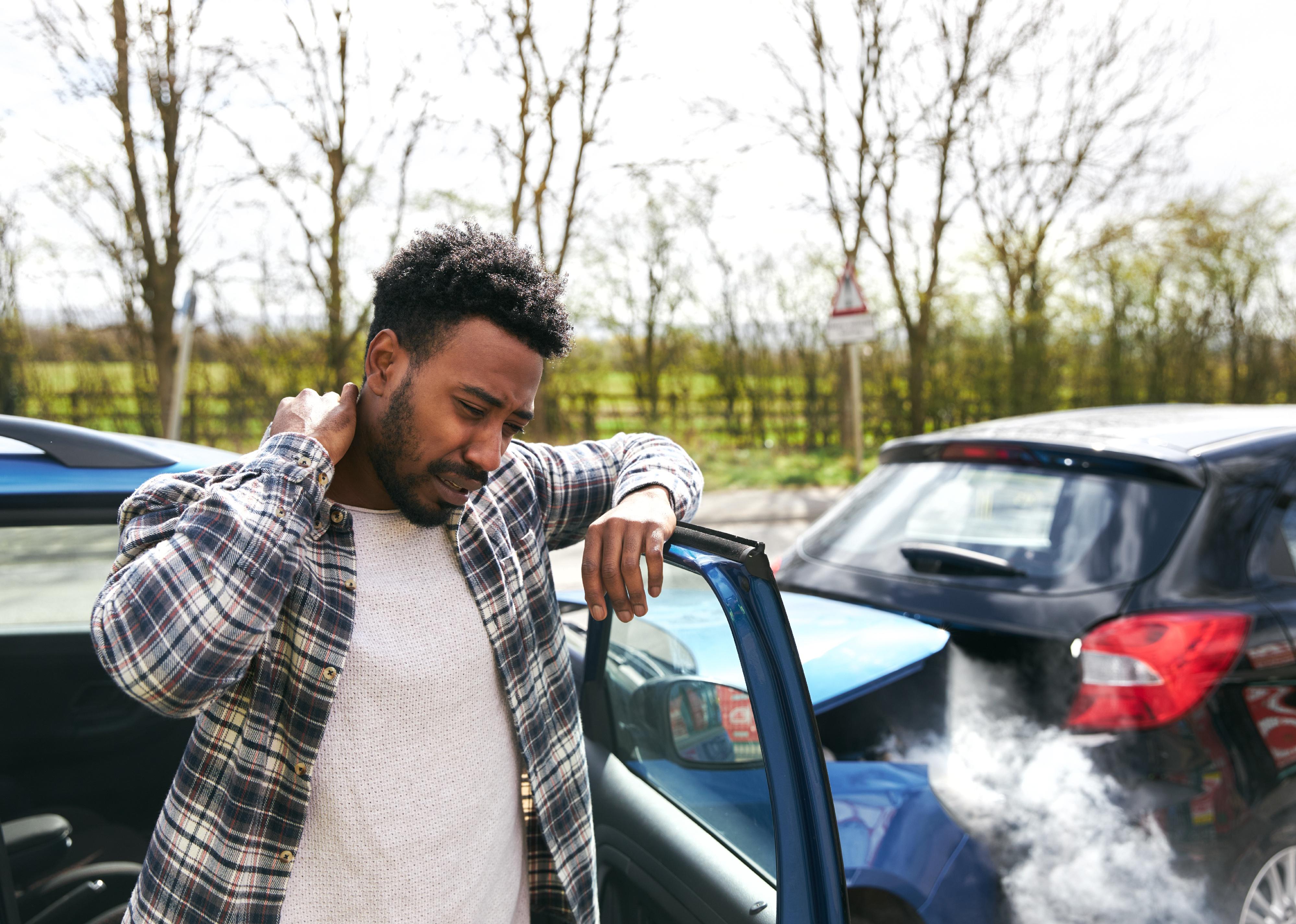 A driver leaning on a car door, rubbing his neck in pain from whiplash injury.