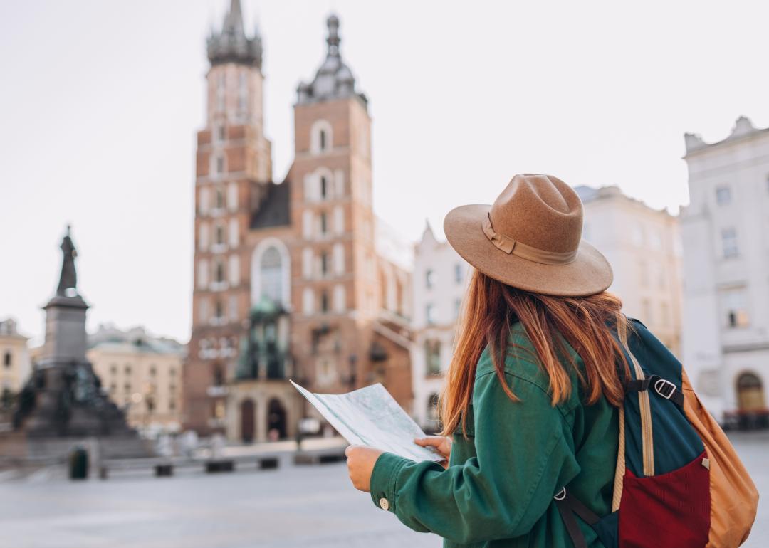 Tourist holding a paper map, looking out onto a city square.